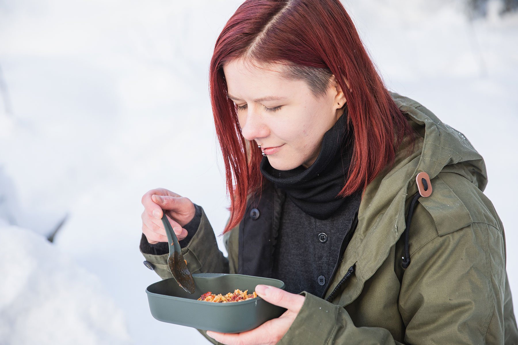 A person holding and looking at a plate of food and holding a spoon above it.