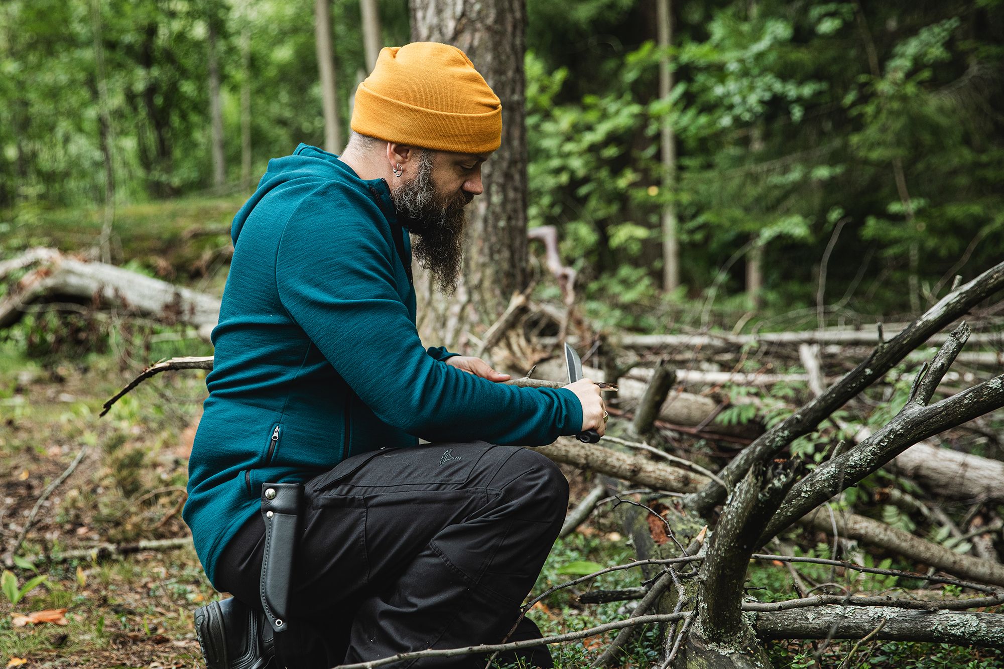 Mies polviseisonnassa metsässä vuolee puuta.